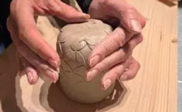 Hands shaping clay on wooden surface.