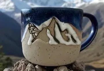 Ceramic mug with mountain design outdoors.