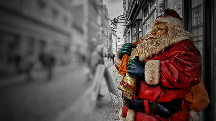 Weihnachtsmann-Statue hält Glocke, Straßenszene im Hintergrund.
