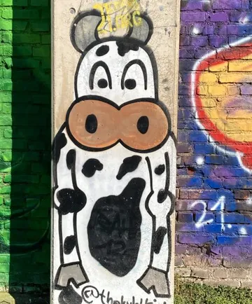 Cartoon cow painted on colorful brick wall.