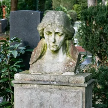Stone bust on grave, surrounded by greenery.