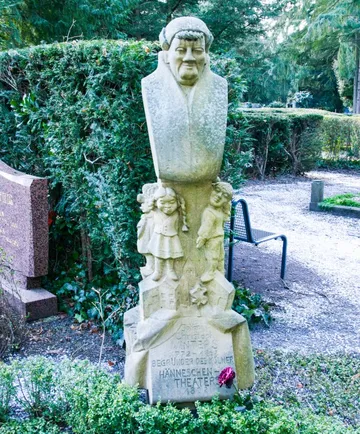 Steinfigur auf Friedhof mit Gravurtext.