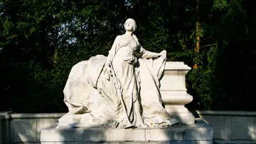 Marble statue in garden, surrounded by trees.