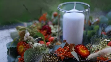 Weiße Kerze auf Blumenarrangement im Freien.