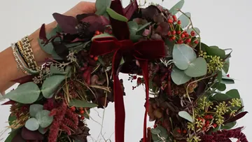 Hand hält floralen Kranz mit roten Beeren.