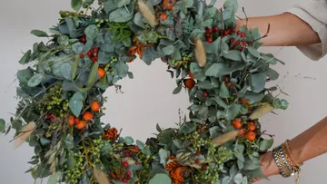 Hands holding a decorative leafy wreath.