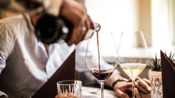Person pouring red wine, restaurant setting.