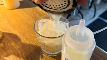 Cocktail being poured over ice in a glass.