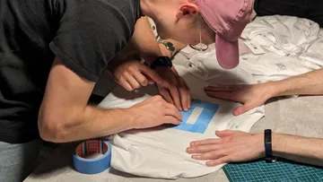 Person klebt Klebeband auf weißes Shirt.