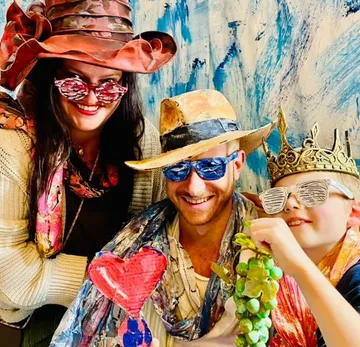 Drei Personen tragen bunte, schräge Kostüme drinnen.