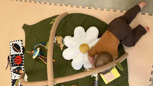 Baby krabbelt auf Spielmatte mit Spielzeug.