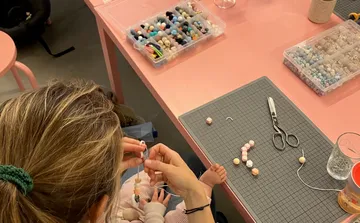 Person bastelt Perlen auf rosa Tisch.