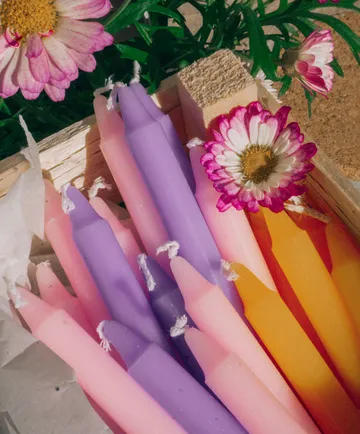 Bunte Kerzen in Holzkiste mit Blumen.