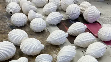 Weiße Keramikmuscheln auf Holztisch, darunter Zeitungen.