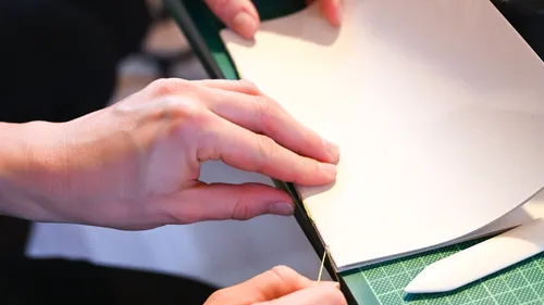 Hands stitching paper sheets together.