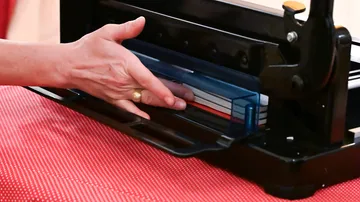 Hand benutzt Maschine auf roter Stoffoberfläche.
