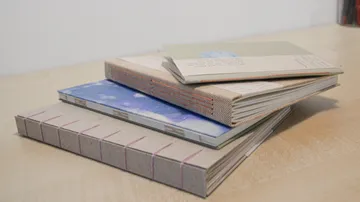 Drei Notizbücher gestapelt, auf Holztisch liegend.