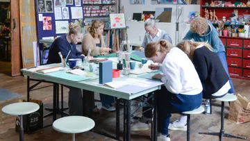 Personen zeichnen an Tischen im Kunststudio.