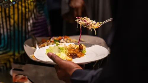 Person serviert Salat auf Teller am Buffet.