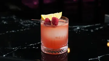 Cocktail mit Himbeeren auf dunkler Theke.