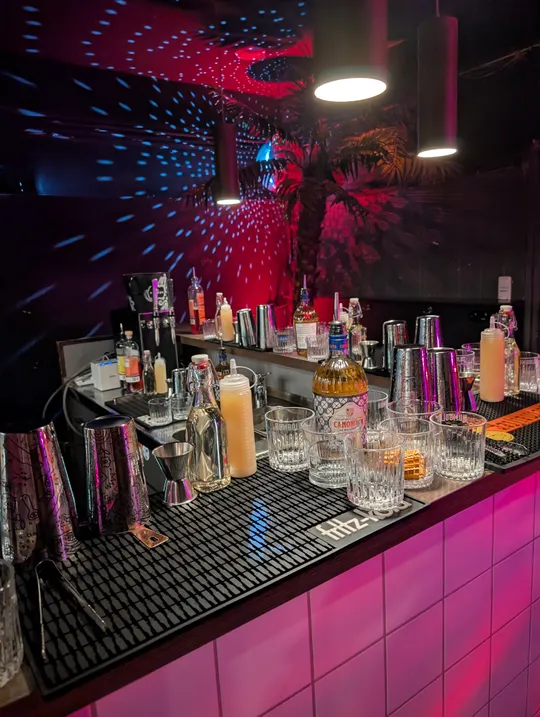 Bar counter with drinks under colorful lights.