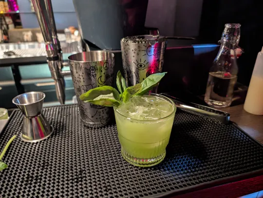 Green cocktail garnished with basil on bar counter.