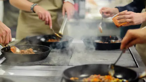 People cooking with frying pans in kitchen.
