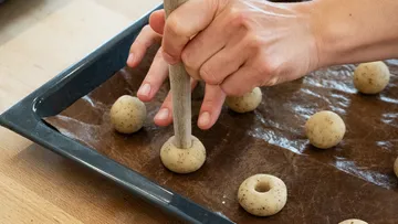 Hände drücken Teigkugeln auf Backblech.