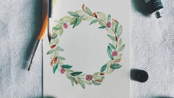Floral wreath watercolor with brushes nearby.