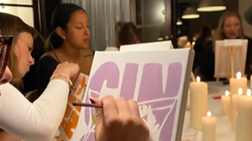 Women painting canvases by candlelight indoors.