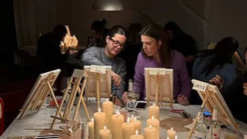 Two people painting at a table with candles.