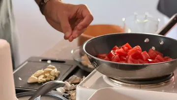 Hand seasoning tomatoes in frying pan.