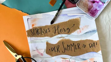 Kunstmaterialien und deutscher Text auf einem Tisch.