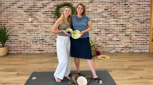 Two women displaying painted plates indoors.