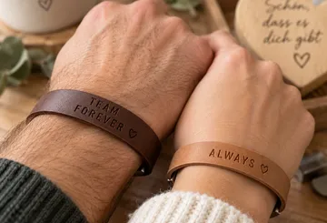 Two wrists wearing engraved leather bracelets.