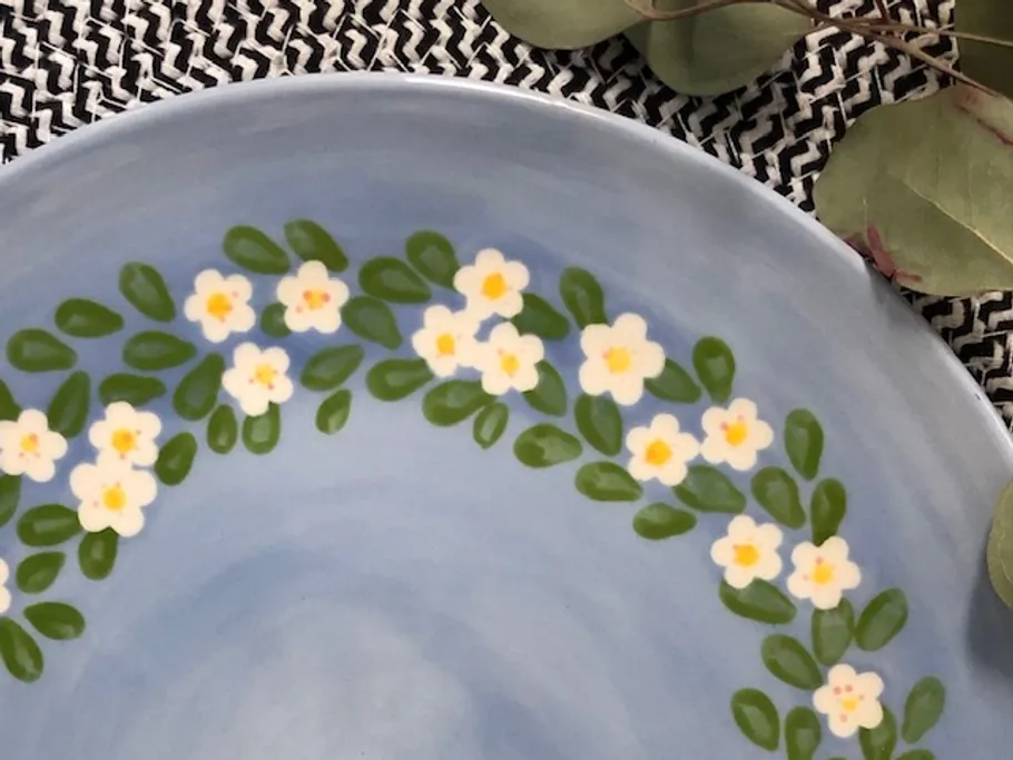 Blauer Teller mit blühendem Blumendesign, auf Textilunterlage.