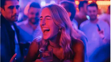 Smiling woman holding drink in crowded bar.