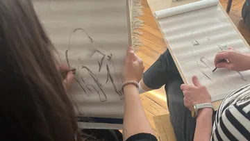 Zwei Personen zeichnen sitzende Figuren drinnen.