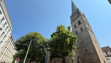 Kirchturm mit Turmspitze vor blauem Himmel.
