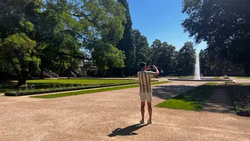 Person photographing fountain in sunny park.