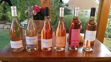 Six wine bottles on wooden table outdoors.