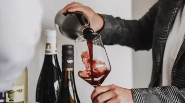 Person gießt Rotwein in Glas drinnen.