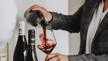 Person gießt Rotwein in ein Glas drinnen.