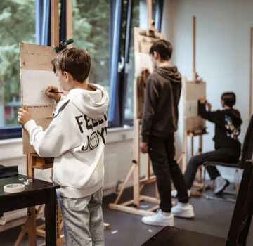 Kinder zeichnen an Staffeleien im Kunstunterricht.
