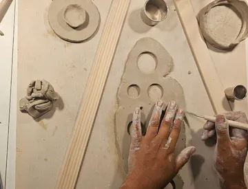 Hände formen Ton auf Holztisch.