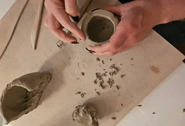 Hände formen Tontopf auf Holztisch.