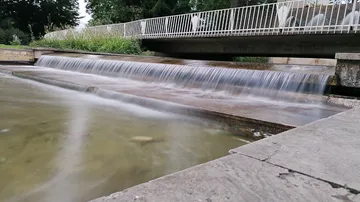 Kleiner Wasserfall fließt unter Brücke im Park.