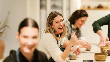 Frauen lachen am Töpfereikurss Tisch.