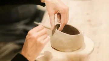 Hände formen Tonvase auf Tisch.