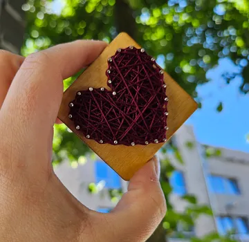 Hand hält Herzkunst vor Bäumen.